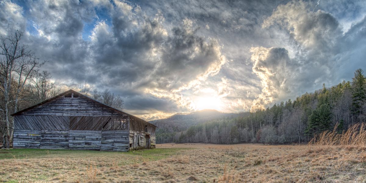 Dramatic skies over a moutain valley with a barn on the forground and Elk in the distance.