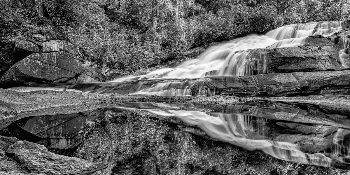 Black and White shot of the lower section of Triple Falls in the DuPont State forest with its reflection in a pool below.